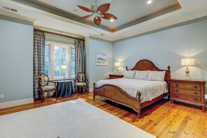 Une chambre à coucher avec un lit en bois, deux tables de chevet, un ventilateur de plafond et une fenêtre avec des rideaux.