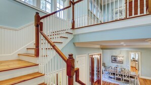 A multi-level wooden staircase with white railings and a dining area with white chairs and a wooden table. - 3rd Row Ocean ~ Five Bedroom Sea Pines Home ~ Private Pool & Spa ~ Sleeps 20 (Hilton Head Island)