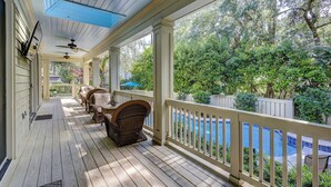 A covered porch with wicker furniture, a pool, and a view of trees. - 3rd Row Ocean ~ Five Bedroom Sea Pines Home ~ Private Pool & Spa ~ Sleeps 20 (Hilton Head Island)
