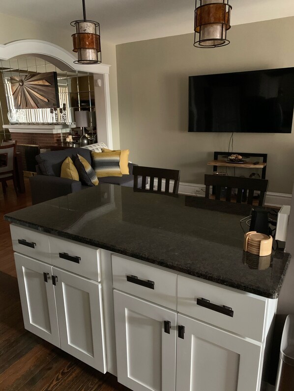 A modern kitchen with a large island, white cabinetry, and a flat-screen TV mounted above the island.
