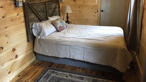 A wooden room with a bed, a lamp, and a door.