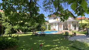 Un patio trasero con piscina, sillas de descanso y un área de terraza cubierta.