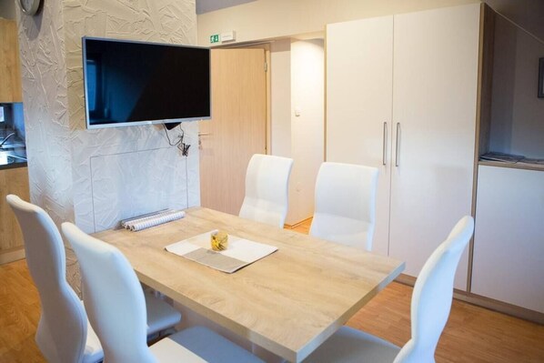 Eine moderne Küche mit einem Holztisch, weißen Stühlen, einem flachbildfernseher an der Wand und weißen Schränken.