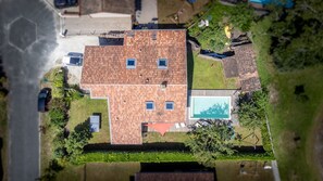 An aerial view of a house with a tiled roof, a swimming pool, and a well-maintained lawn.