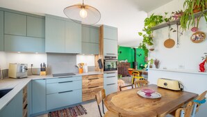 A modern kitchen with light blue cabinets, a wooden dining table, and a hanging light fixture.