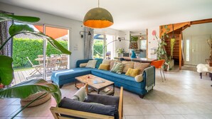 A spacious living room with a blue sofa, a wooden coffee table, and large green plants.
