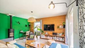 A modern living room with a green wall, wooden paneling, a large TV, and a cozy seating area.