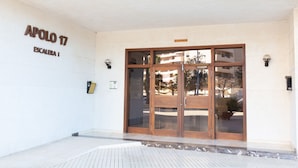 Entrada de un edificio con un letrero que dice 'APOLO 17 ESCALBIA I', puertas de vidrio grandes y una planta en maceta afuera.