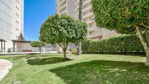 Un patio bien cuidado con césped, algunos árboles y un edificio de varios pisos con balcones al fondo.