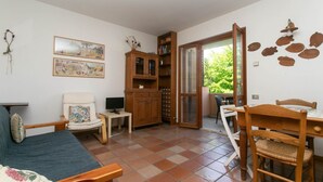 A room with a sofa, a chair, a wooden cabinet, a dining table with chairs, a television, and a window with a view of greenery. - N212 - Numana, four-room apartment in the center with terrace (Numana)