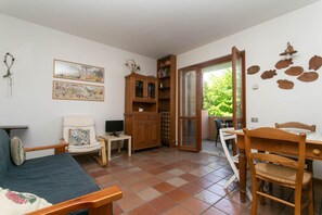 A room with a sofa, a chair, a wooden cabinet, a dining table with chairs, a television, and a window with a view of greenery. - N212 - Numana, four-room apartment in the center with terrace (Numana)