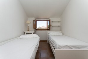 Un petit logement composé d’une seule pièce, comprenant deux lits, une fenêtre, une lampe et une étagère.
