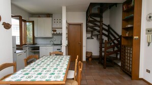 A dining area with a table set for four, a kitchen with white cabinets, and a wooden staircase. - N212 - Numana, four-room apartment in the center with terrace (Numana)