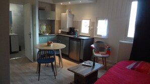 A compact room with a kitchenette, a dining area with a table and chairs, and a bed with a red cover. - "LANDBeautiful beamed apartment in the historic center of Colmar's "Little Venice". (Colmar)