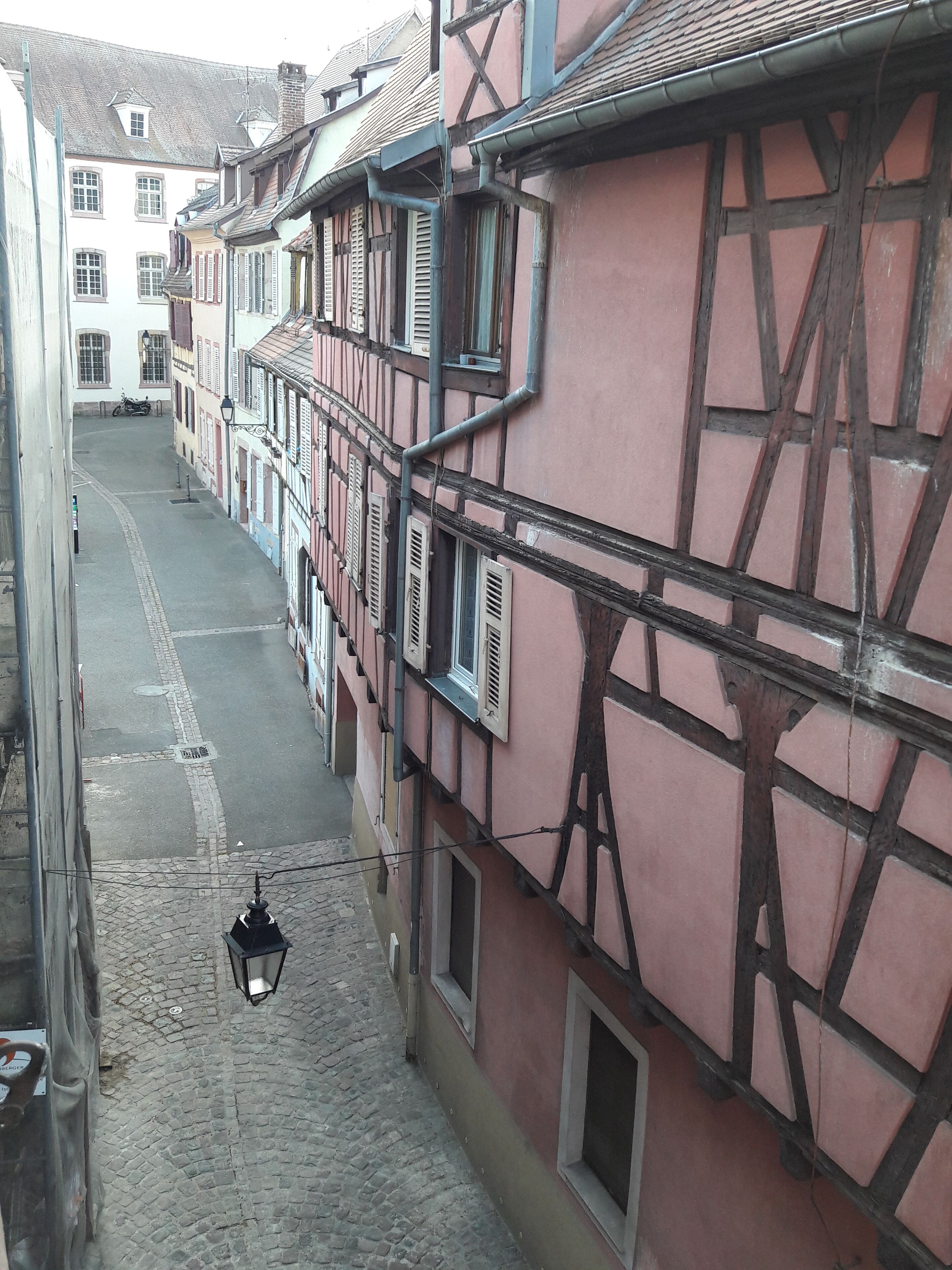 A narrow cobblestone street flanked by traditional half-timbered buildings with exposed wooden beams and shutters.