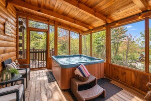 A wooden cabin with a hot tub, deck chairs, and a view of autumn trees.