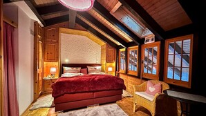 Un dormitorio acogedor de estilo cabaña, con una cama grande, una silla de mimbre y una ventana con vistas.