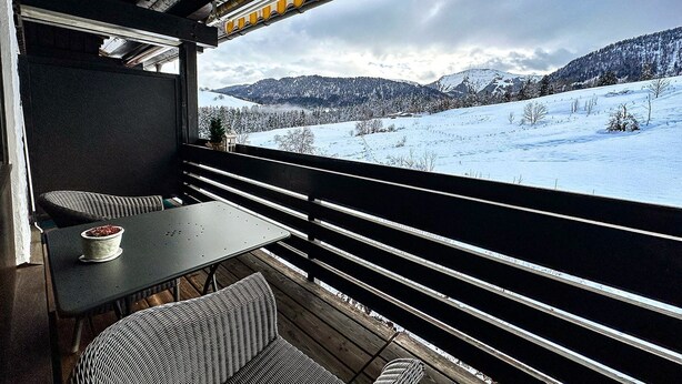 Un rincón acogedor con mesa y sillas, con vistas a un paisaje nevado y montañas.