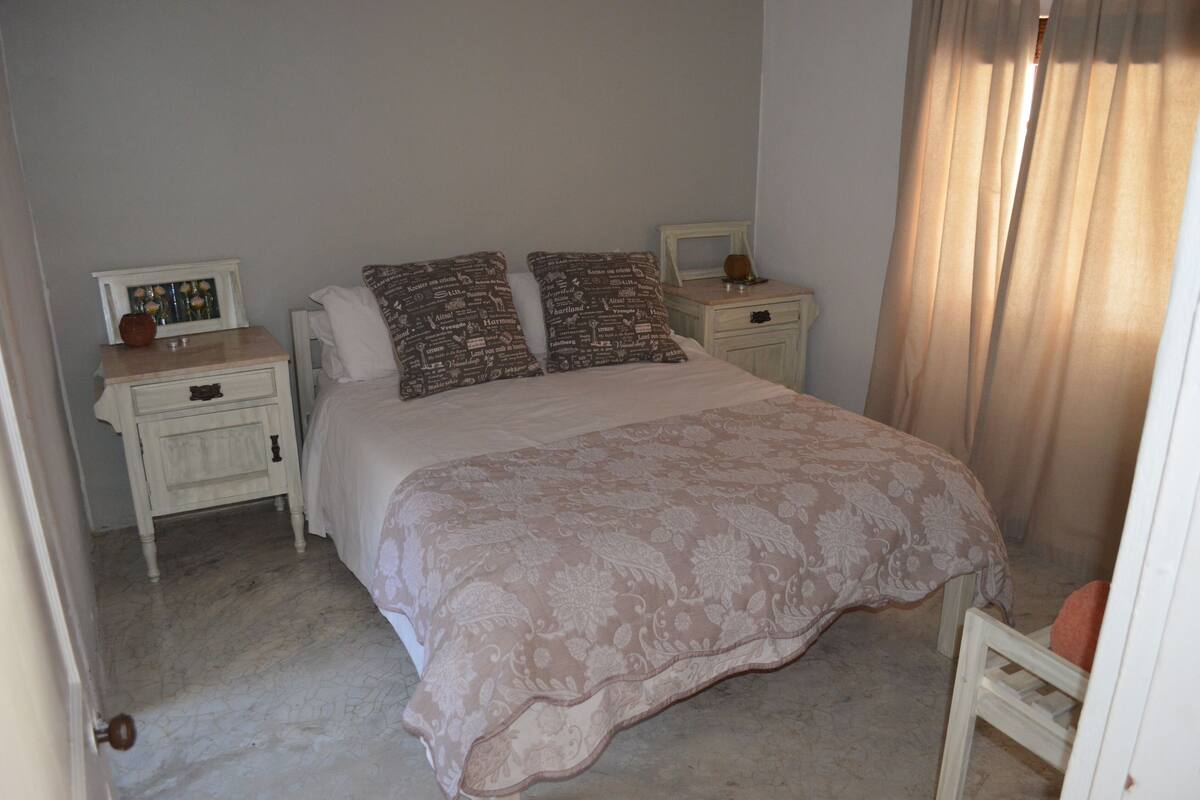 A bedroom with a large bed, two nightstands, a small table, and a chair.