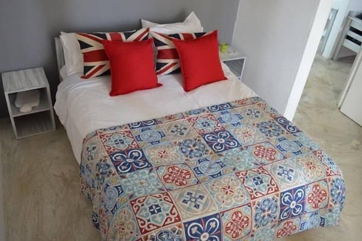 A bed with a colorful patterned bedspread, two red pillows, and a Union Jack pillow.