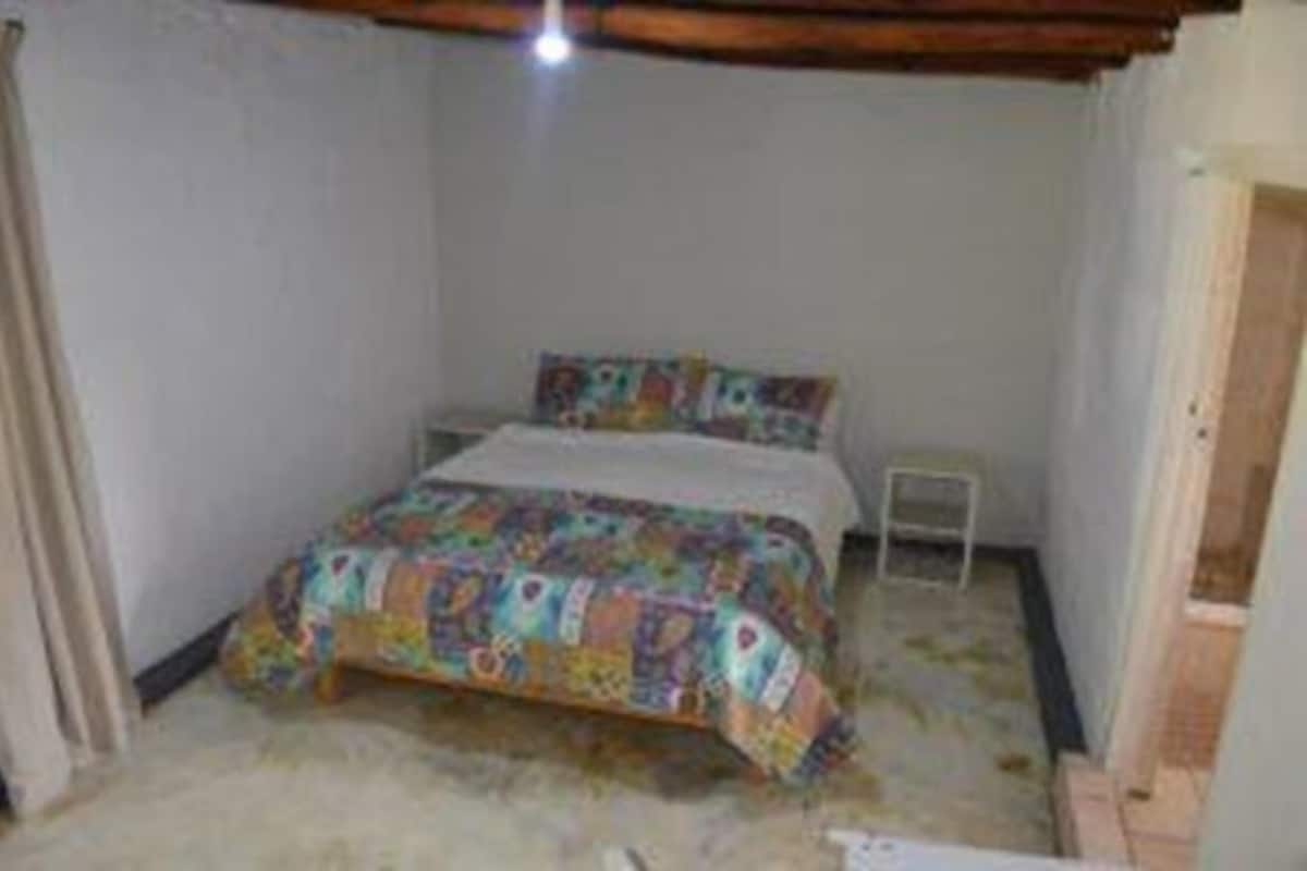 A small, sparsely furnished room with a bed and a nightstand.