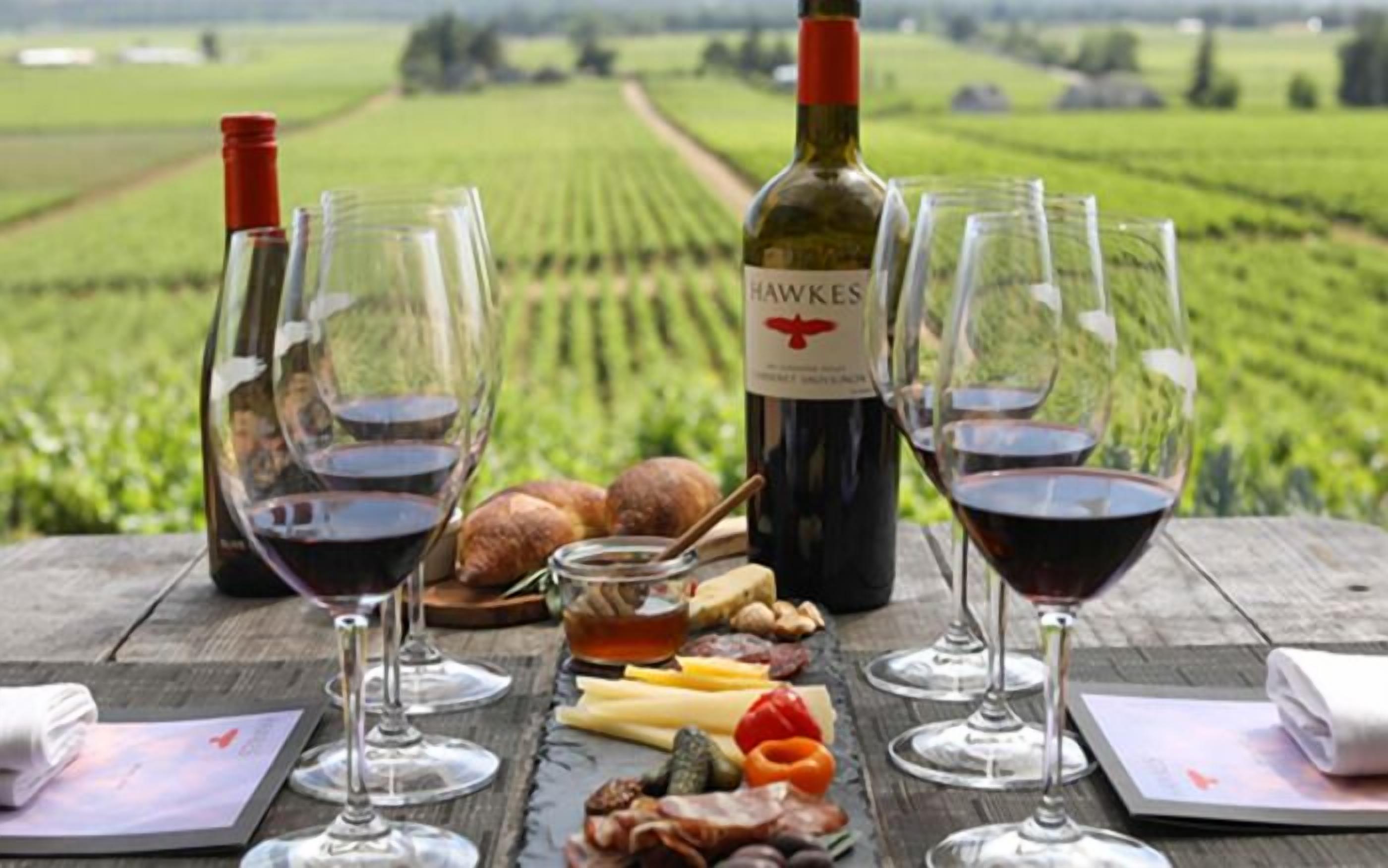A table set with wine glasses, a bottle of Hawkes wine, and an assortment of cheeses and meats.