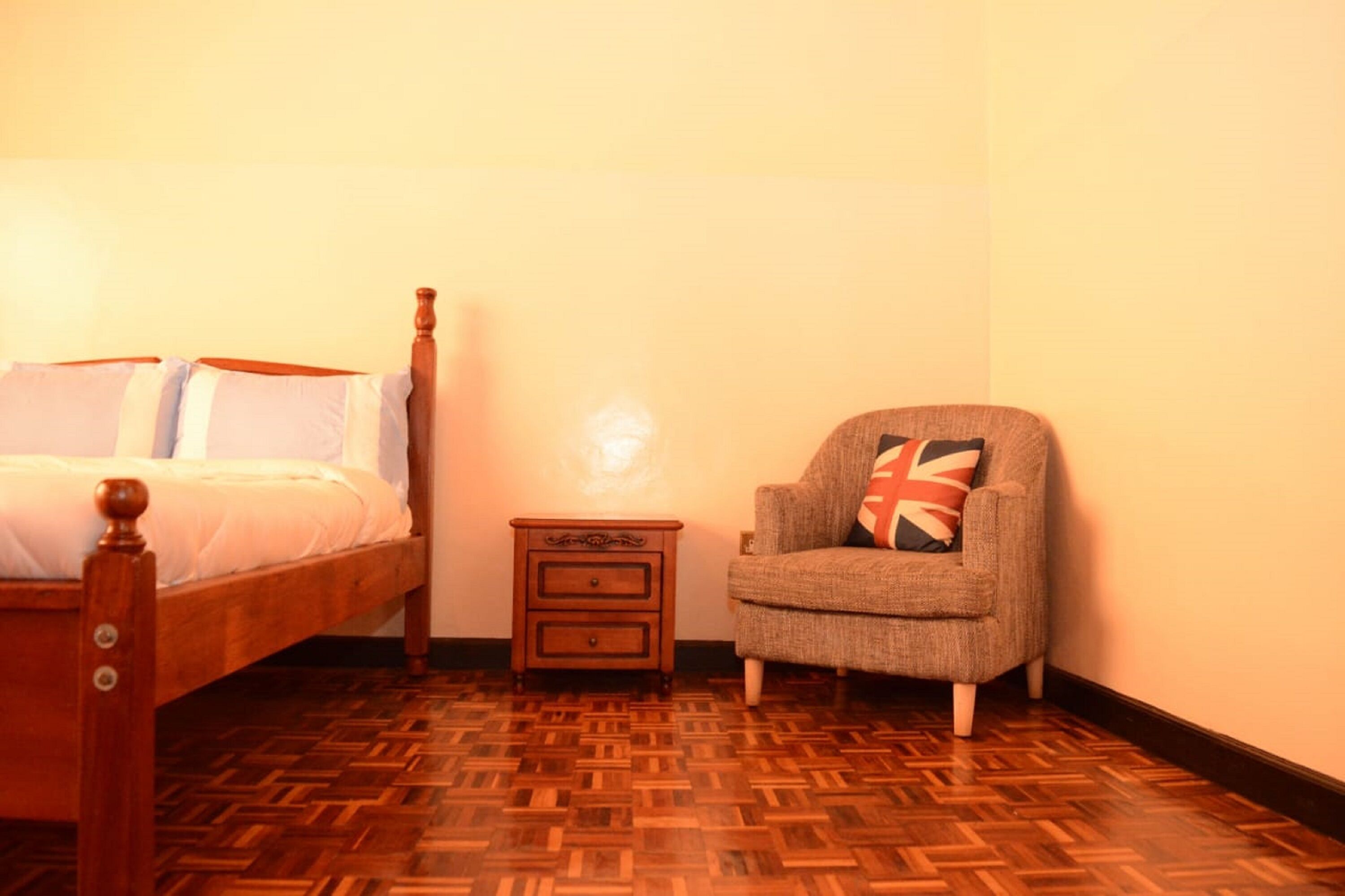 A bedroom with a wooden bed, a nightstand, and a chair with a Union Jack pillow.