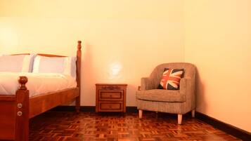 A bedroom with a wooden bed, a nightstand, and a chair with a Union Jack pillow.