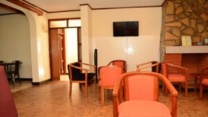 Un vestíbulo de hotel con sillas de madera y un sofá rojo, un televisor de pantalla plana montado en la pared y una chimenea de piedra.