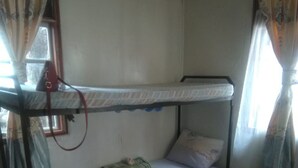 A small, single-bunk room with a patterned floor, a red rug, and curtains on the windows. - Murbs Hostel (Kisumu)