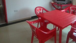 A dining area with a red table and chairs, a painting on the wall, and a television on a stand. - Murbs Hostel (Kisumu)
