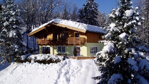 Eine Holzhütte mit Balkon, umgeben von schneebedeckten Bäumen und einem klaren Himmel.