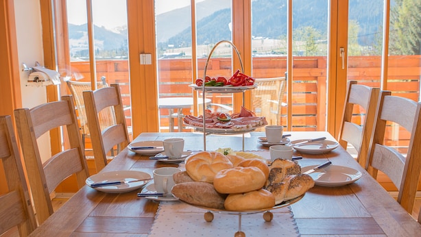 Ein Holzespeisetisch mit Tellern, Tassen und einem Brotkorb, mit Blick auf eine Berglandschaft.