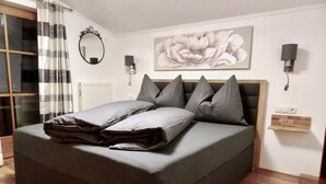 Ein modernes Schlafzimmer mit einem großen Bett, Holzboden, einem wandmontierten Spiegel und einem floralen Gemälde.