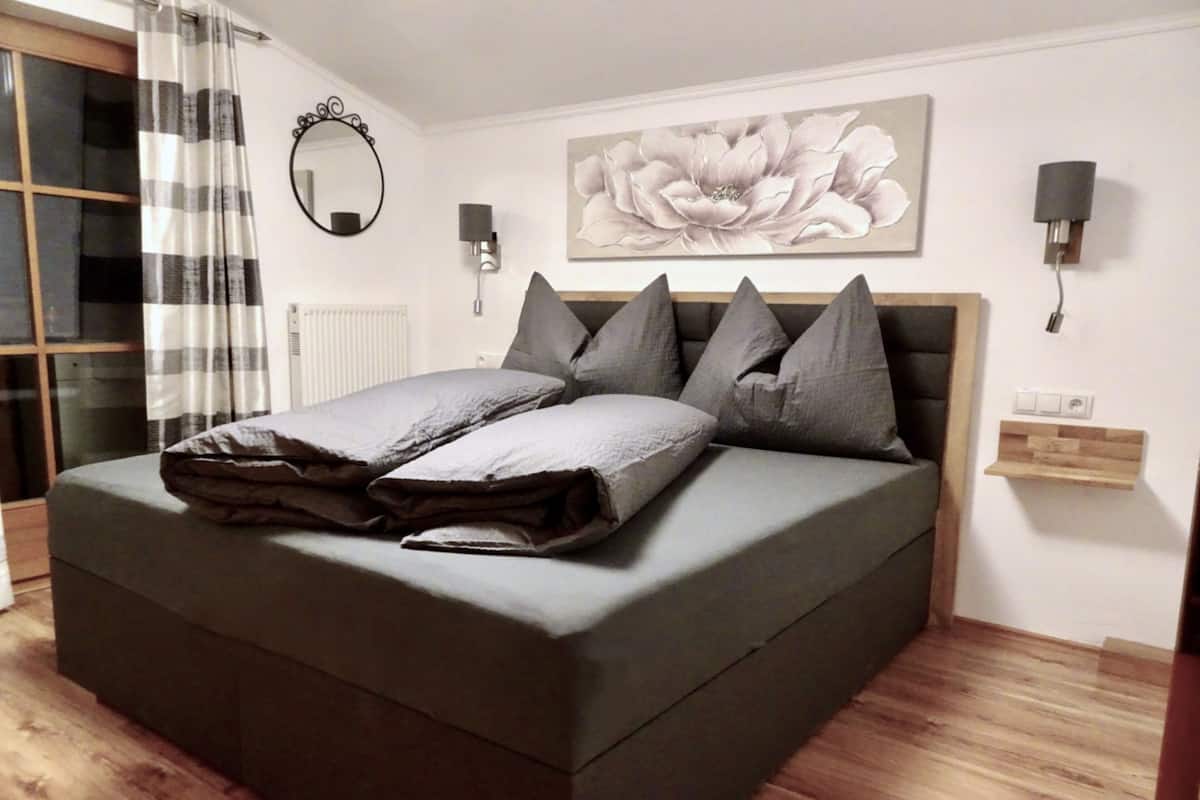 Ein modernes Schlafzimmer mit einem großen Bett, Holzboden, einem wandmontierten Spiegel und einem floralen Gemälde.
