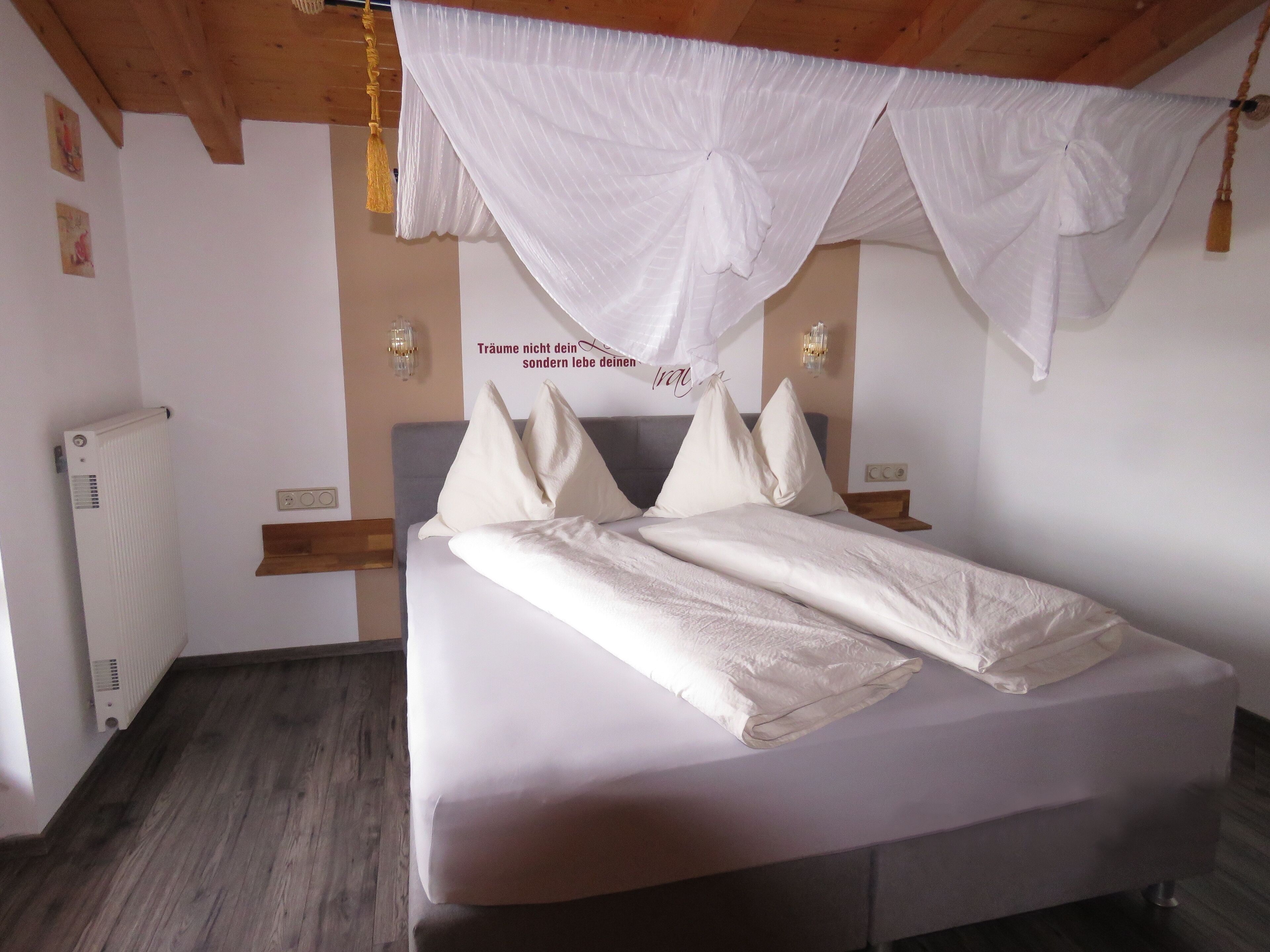A bedroom with a bed, white curtains, and a wall-mounted light fixture.