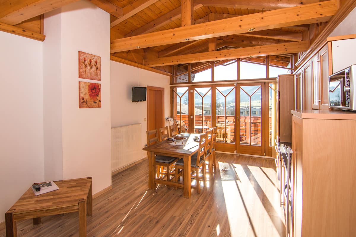 Ein Essbereich aus Holz mit einem Tisch und Stühlen, ein kleiner Tisch mit einer Zeitschrift und ein Fernseher an der Wand.
