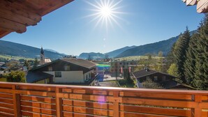 Ein Balkon mit Holzbalkon, der auf ein Dorf mit Häusern, eine Kirche und Berge im Hintergrund blickt.