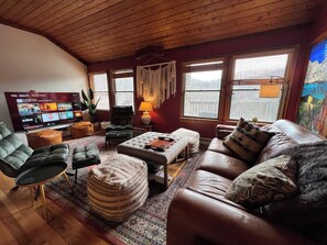 Een gezellige woonkamer met een leren bank, een groene fauteuil, een salontafel en een televisie waarop een programma wordt vertoond.