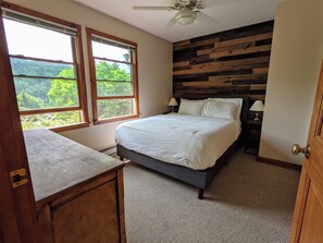 A bedroom with a bed, two windows, a ceiling fan, and a wooden wall panel.