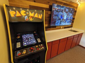 Una màquina recreativa de Pac-Man amb un joc de laberint, un televisió que mostra un partit de bàsquet i armaris vermells.