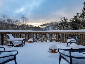 A snow-covered deck with outdoor seating and a view of a forested area.