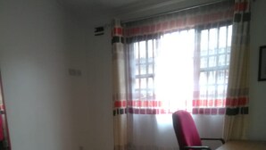 A hotel room with a bed, a chair, a table, and a window with curtains. - Rokas Hotel (Migori)