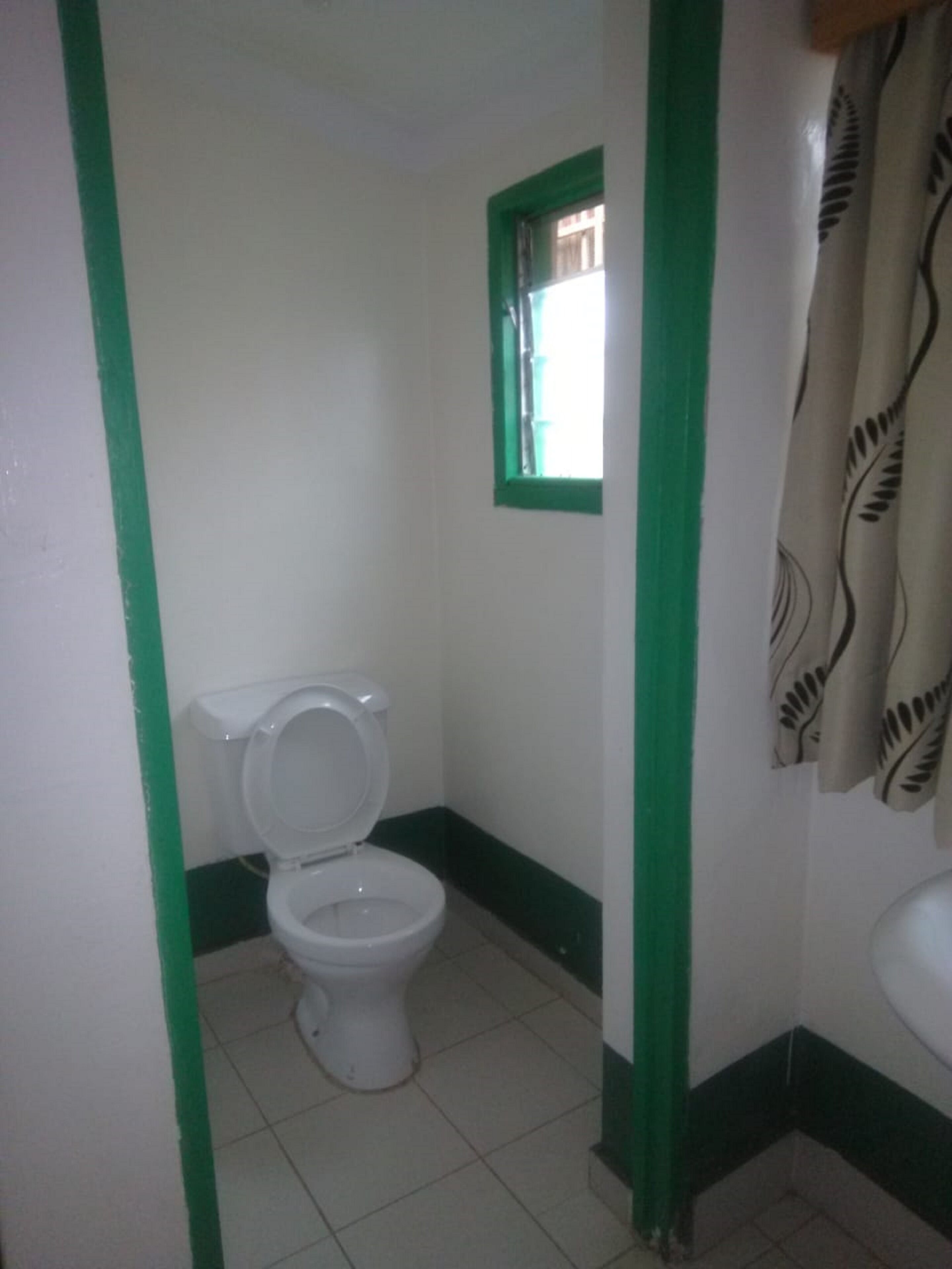 Une petite salle de bain simple, équipée de toilettes, d’une fenêtre et d’un rideau de douche.