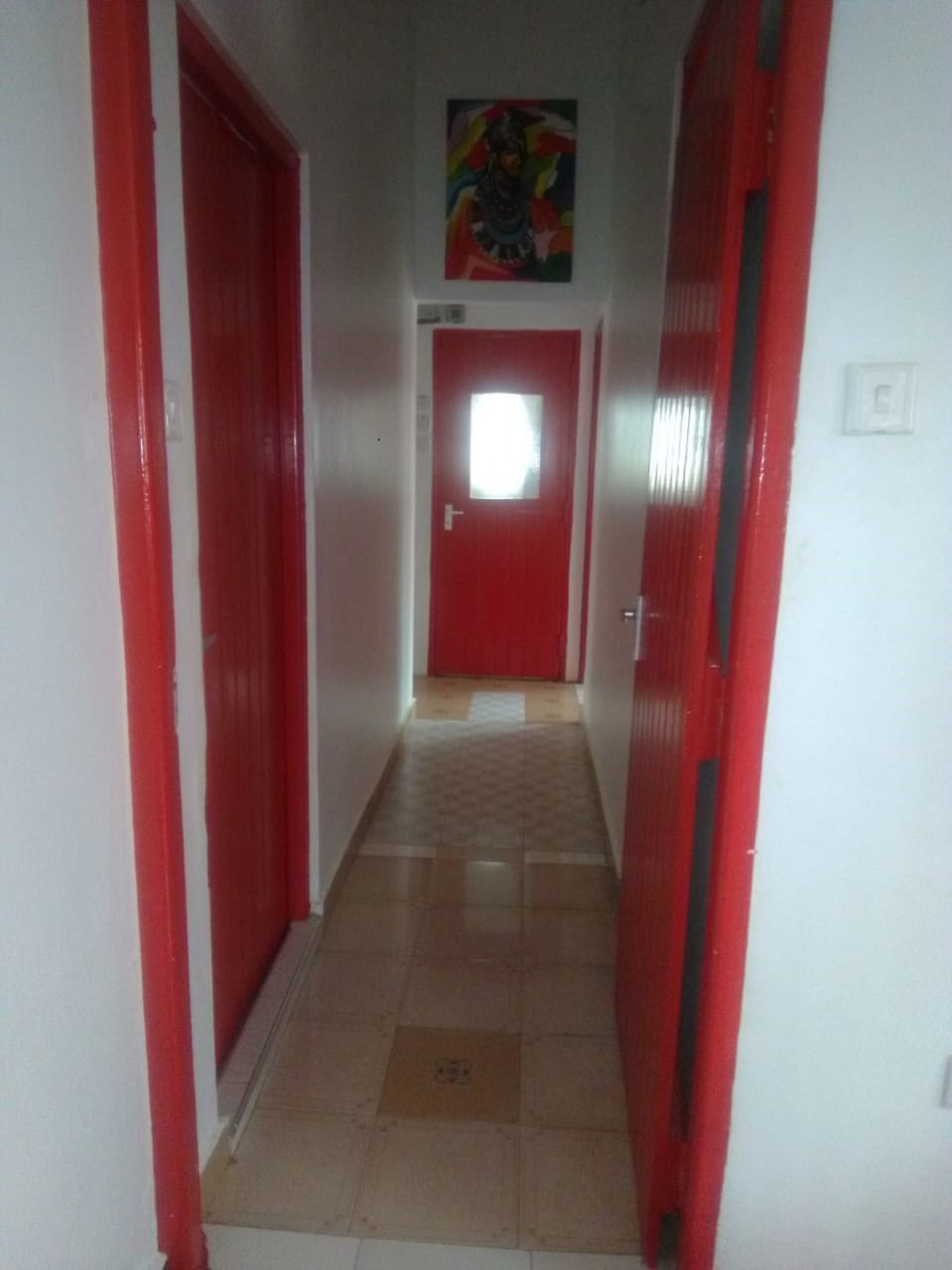 Un pasillo estrecho con puertas rojas a ambos lados y una puerta roja al final.