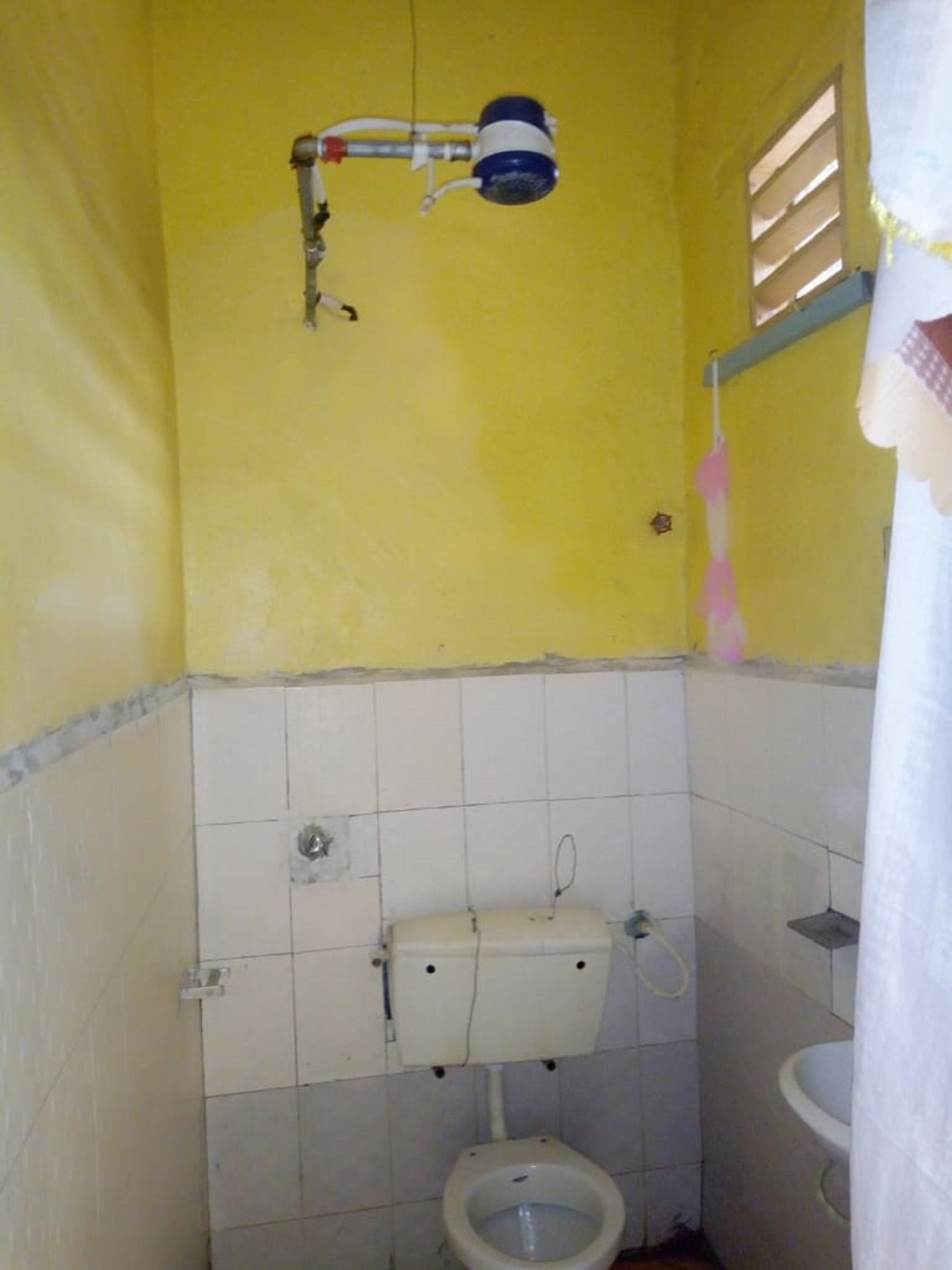 A small, yellow-walled bathroom with a toilet, a water heater, and a shower head.