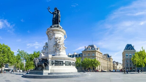 A large outdoor statue in a public square with classical architecture in the background.