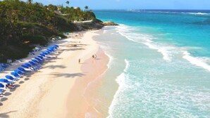 A beach with clear turquoise waters, a sandy shore, and a row of blue umbrellas. - Barbados Luxury Ocean Front Villa ~ 7 Bedroom Suites ~ 7 Private Bathrooms (St Philip)