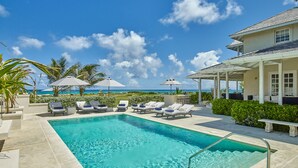 A pool area with lounge chairs and umbrellas, a clear blue sky, and a view of the ocean. - Barbados Luxury Ocean Front Villa ~ 7 Bedroom Suites ~ 7 Private Bathrooms (St Philip)
