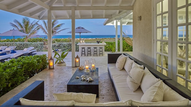 An outdoor patio with a sofa, table, and umbrellas, overlooking a beach. - Barbados Luxury Ocean Front Villa ~ 7 Bedroom Suites ~ 7 Private Bathrooms (St Philip)